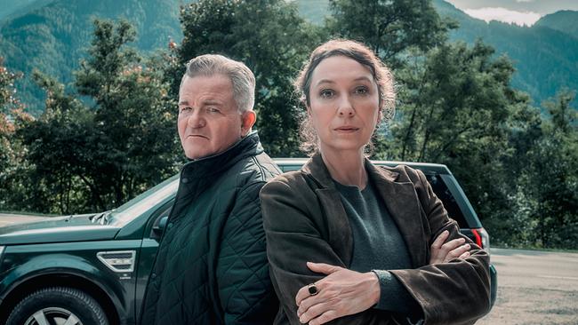 © ORF/Rundfilm/Nikolett Kustos Ursula Strauss als Fanny Gruber und Cornelius Obonya als Benedikt Renner stehen vor einem grünen Geländewagen und blicken direkt in die Kamera, im Hintergrund Bäume und bewaldete Berge