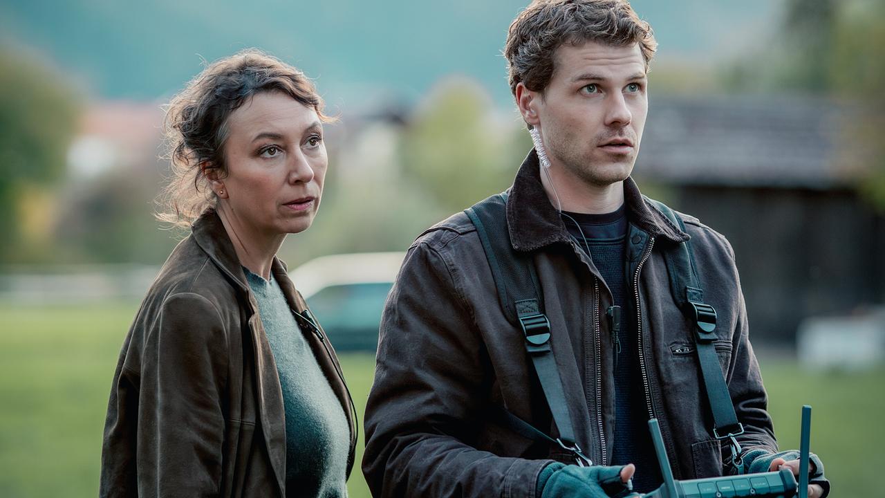 © ORF/Rundfilm/Nikolett Kustos Ursula Strauss als Fanny Gruber und Noah L. Perktold als Tobi Gruber, die beiden stehen im Freien, er bedient die Fernbedienung einer Drohne, sie steht hinter ihm und blickt in dieselbe Richtung