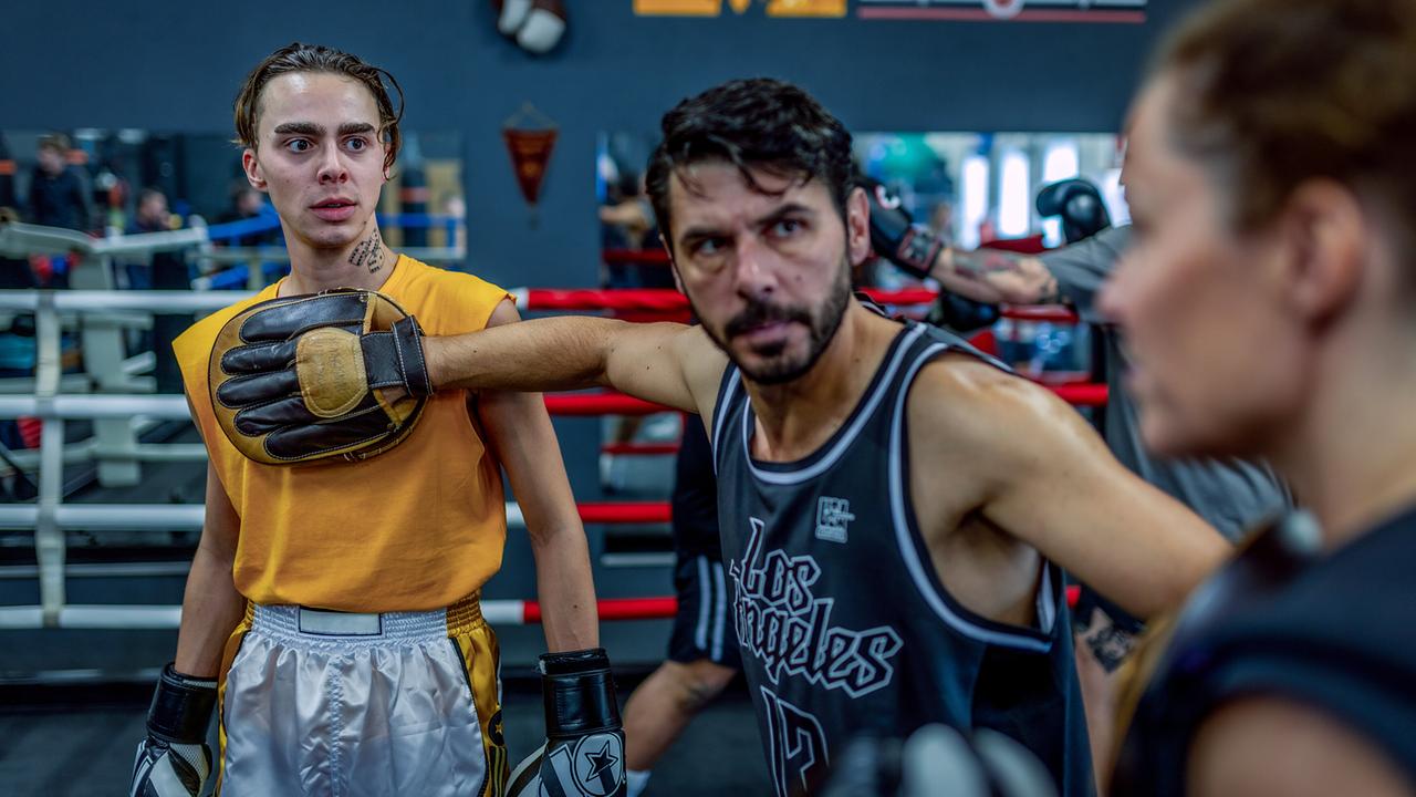 Im Boxring in einem Boxstudio steht Dolce zwischen Marco Relli und Lisa Kuen und stoppt sie mit seinen Händen.