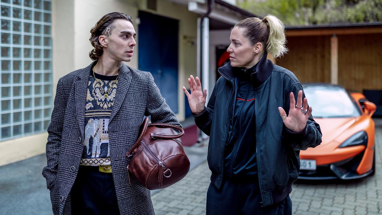 Marco Relli und Lisa Kuen unterhalten sich vor einer Hauseinfahrt, im Hintergrund steht ein sportliches Auto.