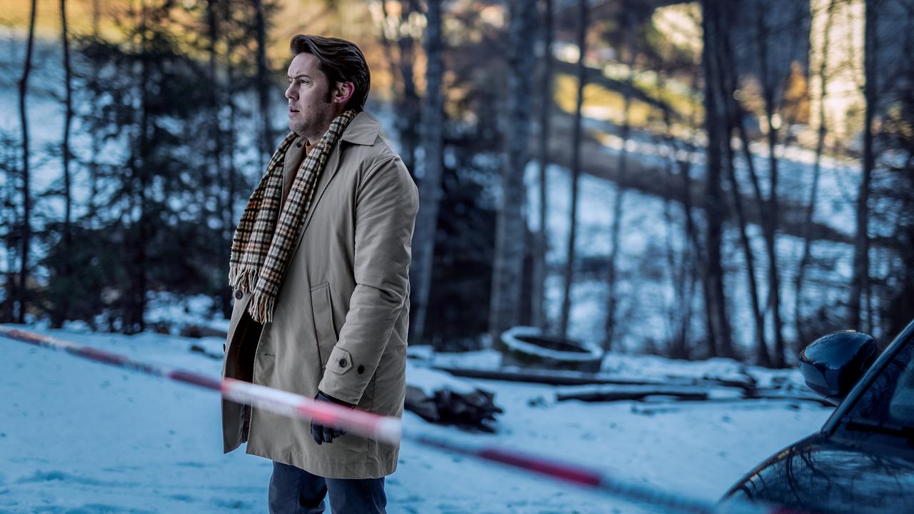 Alex Yüsüf-Demir steht tagsüber im winterlichen Waldgebiet hinter einer Absperrung.