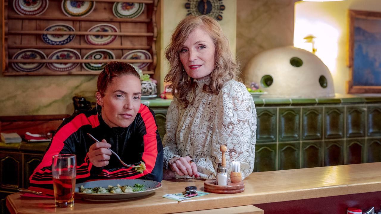 Lisa Kuen sitzt in einer gemütlichen Stube am Tresen beim Essen, während Caterina Relli neben ihr steht.