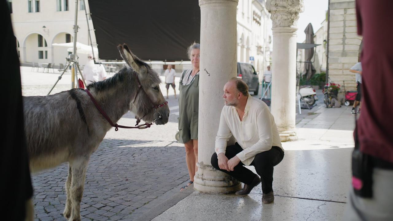 © ORF/AÖF Thomas Stipsits hockt neben einem Esel in einem italienischen Arkadengang bei den Dreharbeiten zu "Italien oder Non mio Esolo".