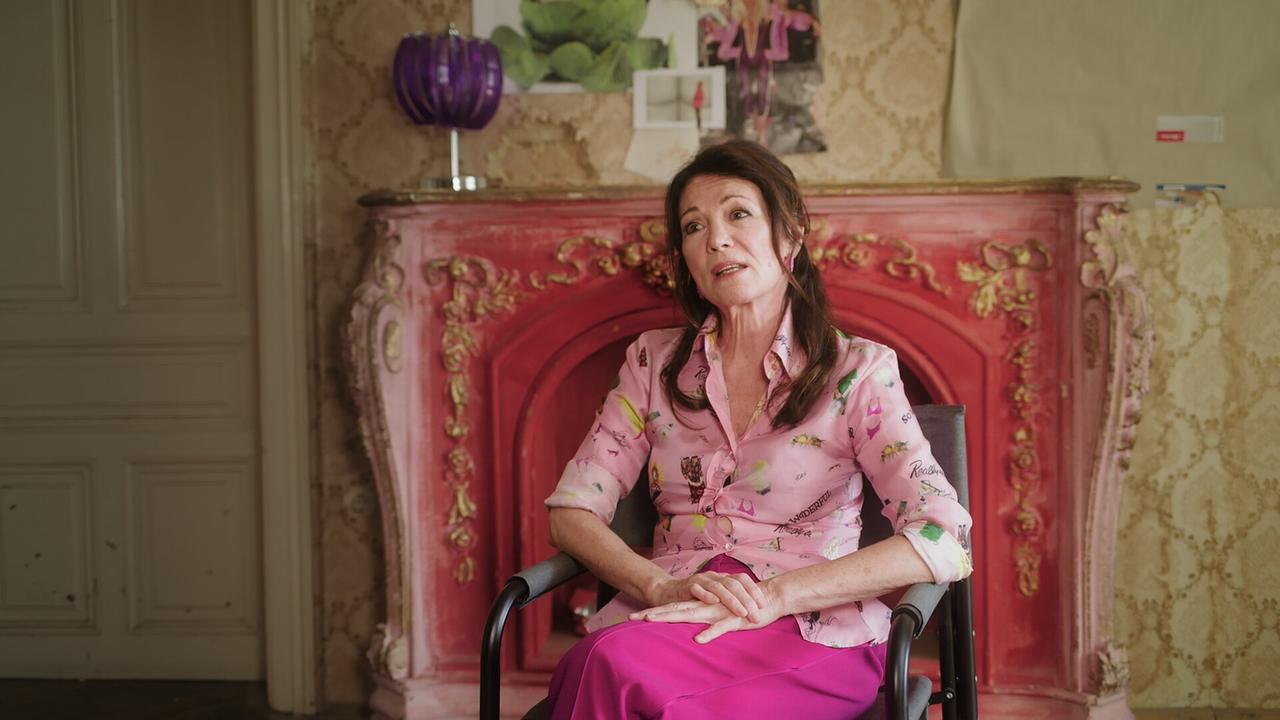 © ORF/AÖF Iris Berben sitzt sitzt vor einem auffällig rosafarbenen, reich verzierten Kamin beim Interview zu "Sentimental Fail Club"