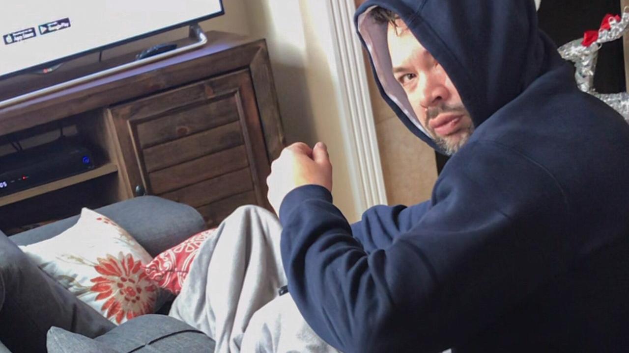 Brandon Johnson in einem Hoodie in einem Wohnzimmer vor einem Flat-Screen-Fernseher, fragend dreht er sich um und blickt erstaunt in die Kamera
