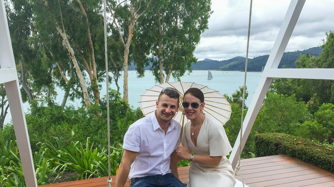 Melissa Caddick mit ihrem Ehemann Anthony Koletti auf einer Schaukel auf einer Aussichtsterrasse - hinter ihnen eine paradiesische Meeresbucht