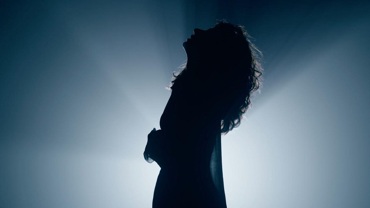  Silhouette einer Frau mit langen Haaren vor einem Lichtspot