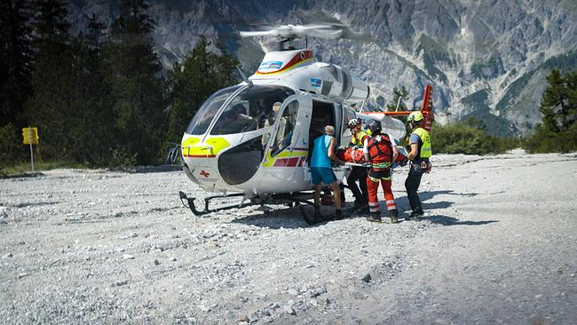 © ORF/BR/Timeline Production Ein Rettungsteam der Bergwacht Ramsau bringt auf einem steinigen Gelände vor einer Bergkulisse eine Person auf einer Trage in einen Hubschrauber.