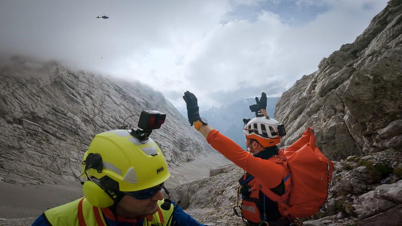 Einsatz der Bergwacht Ramsau: Die Bergretter Christian Datzmann und Michael Renner, beide in Schutzkleidung, koordinieren in einer steilen, nebelverhangenen Felsrinne den Einsatz eines Hubschraubers.