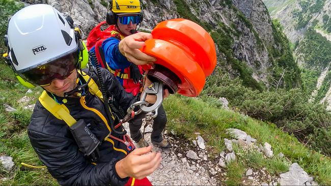 © ORF/BR/Timeline Production Notarzt Bernhard Kraus (vorne) und ein weiterer Bergretter hinter ihm bereiten an einem steilen alpinen Hang die Seilbergung vor.