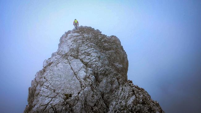 Einsatz der Bergwacht Ramsau am Watzmann: Eine einzelne Bergretter steht auf einem schroffen Felsgrat im Nebel, hoch über der Landschaft, umgeben von blau-grauer, wolkiger Atmosphäre.
