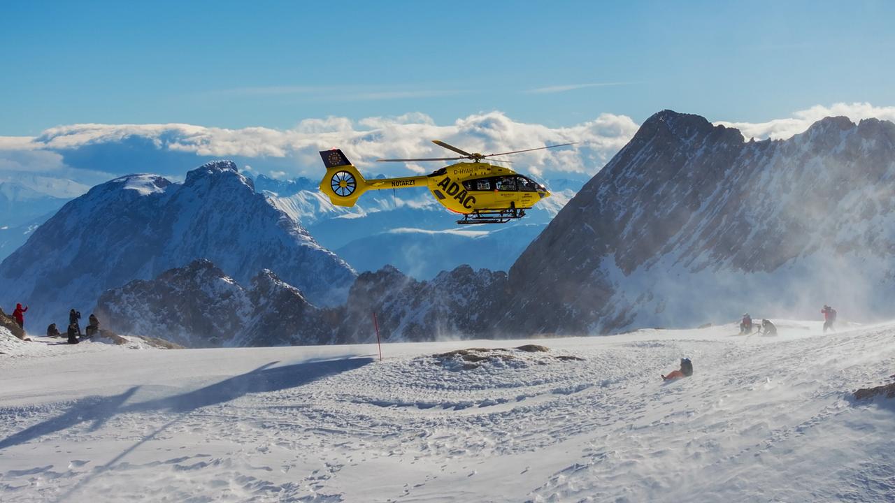 Ein gelber Rettungshubschrauber der Bergwacht Grainau im Einsatz über einer verschneiten Berglandschaft