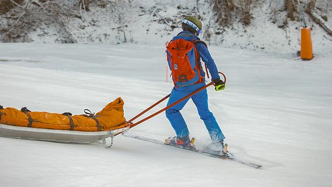 Eine Einsatzkraft der Bergwacht Grainau auf Skiern, die eine verletzte Person in einem Rettungsschlitten über die Piste zieht.