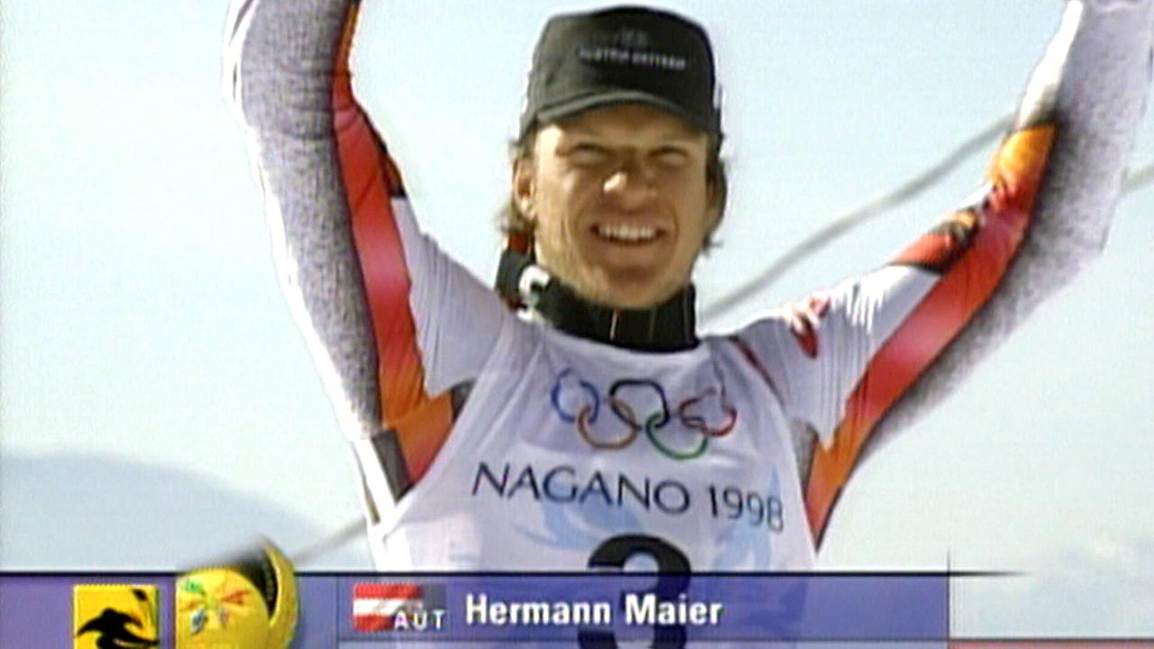 Hermann Maier im rot‑weißen Anorak jubelt auf einem Podium bei den Olympischen Winterspielen in Nagano 1998 über eine Goldmedaille.