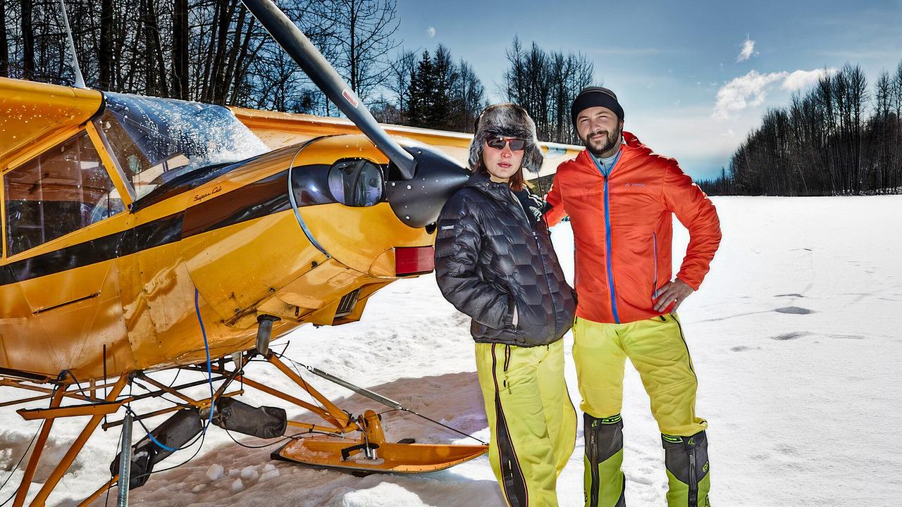 © ORF/ARD Plus/WDR/Mike Fuchs Sylvia M. und Mike Fuchs zu Beginn ihrer Expedition zum Denali, dem höchsten Berg von Alaska, in verschneiter Landschaft stehen sie vor einem gelben Propellerflugzeug mit Kufen und blicken in die Kamera
