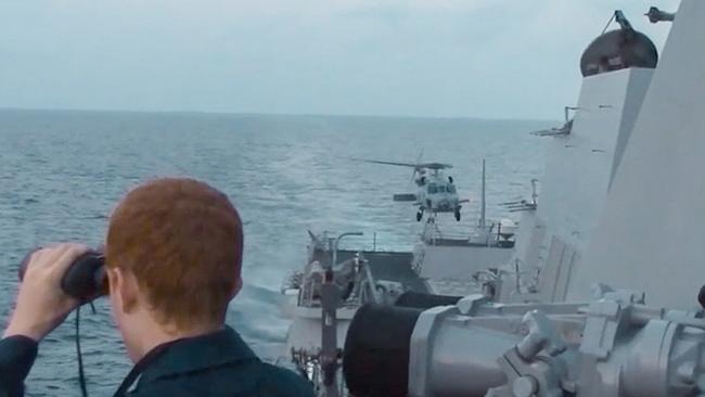 Ein Kriegschiff auf hoher See, ein Mann ist mit dem Feldglas auf der Suche, im Hintergrund landet ein Hubschaurber auf dem Schiff