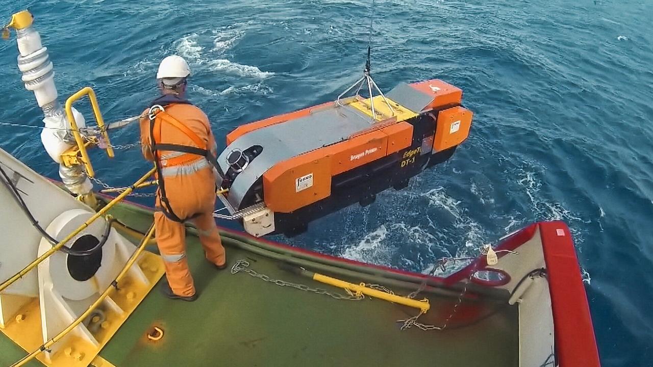 Ein Mann in orangefarbenem Overall steht an der Reling eines Schiffes und hilft einen Untersuchungsapparat ins Wasser abzusenken