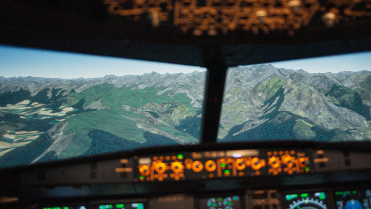 Blick aus der Cockpit eines Flugsimulators, auf den Bildschirmen die südfranzösischen Alpen davor orange-leuchtende Instrumente