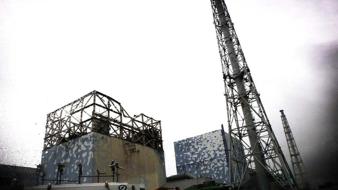 Zwei große würfelförmige Gebäude mit Kaminen, das vordere Gebäude ist zerstört, im oberen Bereich ist die Metallstruktur freigelegt, die Verkleidung fehlt