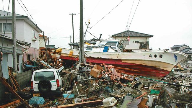 In Sendai ist ein Fischkutter auf die Straße zwischen den Wohnhäusern geschwemmt worden, im Vordergrund ein Auto und eine Menge zerstörter Möbeln