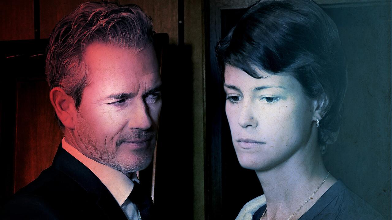 Ein Mann im Anzug, Hemd und Krawatte blickt auf eine Frau, die ihren Blick betrübt senkt, während er rot beleuchtet wird, ist sie in kaltem Licht