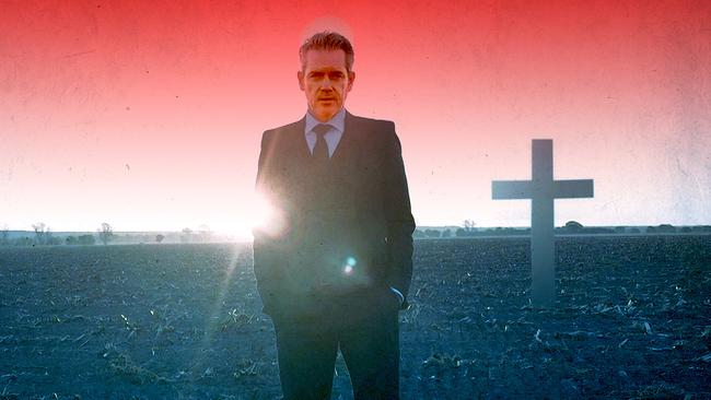 Ein Mann im dunklen Anzug, blauem Hemd mit Krawatte, steht auf einem Feld, hinter ihm ein großes Kreuz vor tiefrot eingefärbtem Himmel