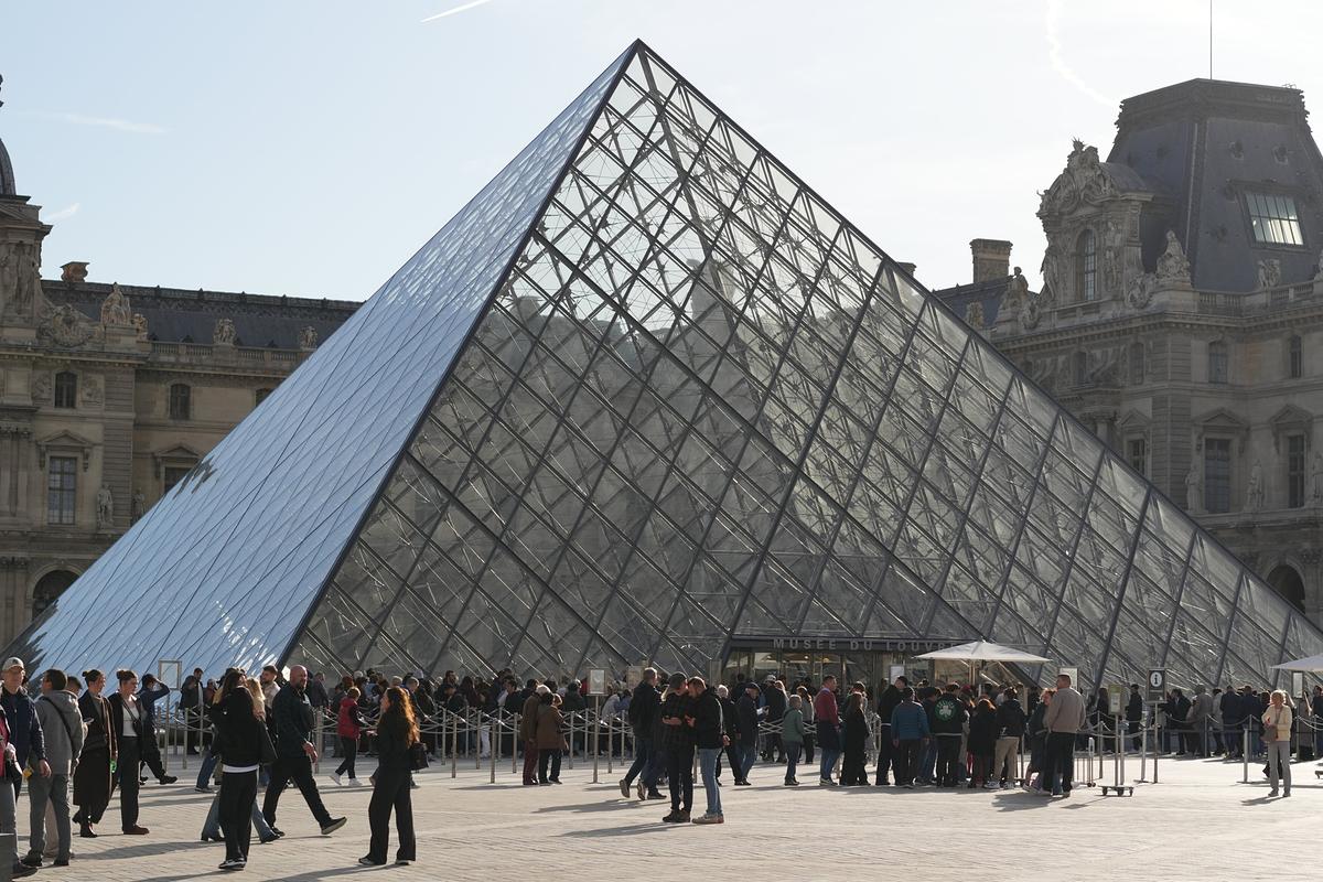 Die gläserne Pyramide im Innenhof des Louvre, auf dem sonnigen Platz stehen viele Menschen