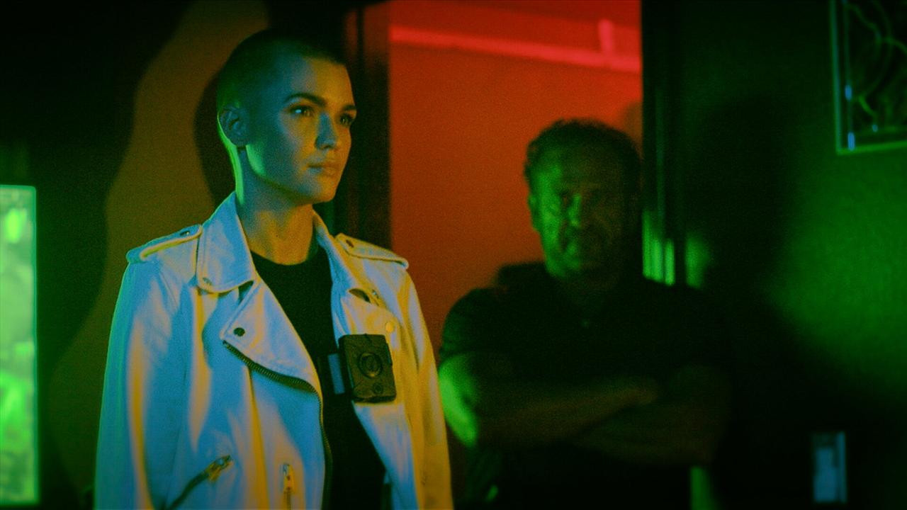 © ORF/Wild Bunch Germany GmbH/David R. Gaynes Ruby Rose steht als Victoria in einem dunklen in grün und rot beleuchteten Raum, sie trägt einen weißen Mantel, darunter ein schwarzes Shirt