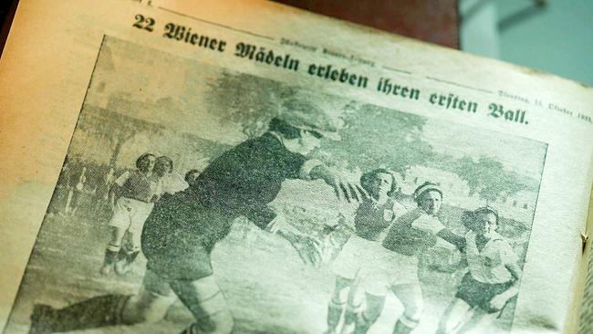 Eine vergilbte Zeitungsseite zeigt die Schlagzeile "22 Wiener Mädeln erleben ihren ersten Ball", darunter ein historisches Foto von Mädchen, die bei einem frühen Fußballspiel einem Ball nachjagen.