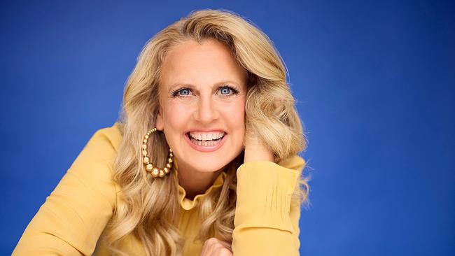 Porträtfoto von der lächelnden Barbara Schöneberger in gelber Bluse vor blauem Hintergrund 