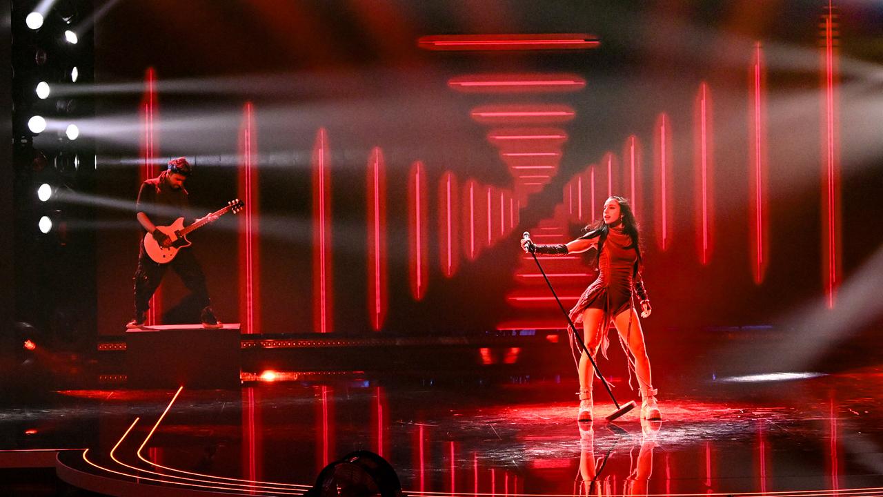 Anna-Sophie steht mit einem Standmikrofon auf einer Bühne mit roten Lichttunneln, links begleitet von einem Gitarristen unter starken Spotlights.