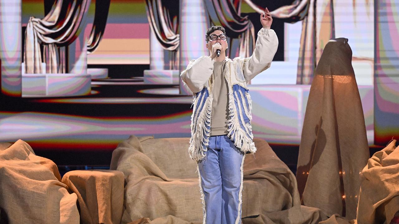 Philip Piller in hellem Outfit performt auf einer Bühne mit beigefarbenen Stofflandschaften und einer abstrakten, pastellfarbenen Kulisse.