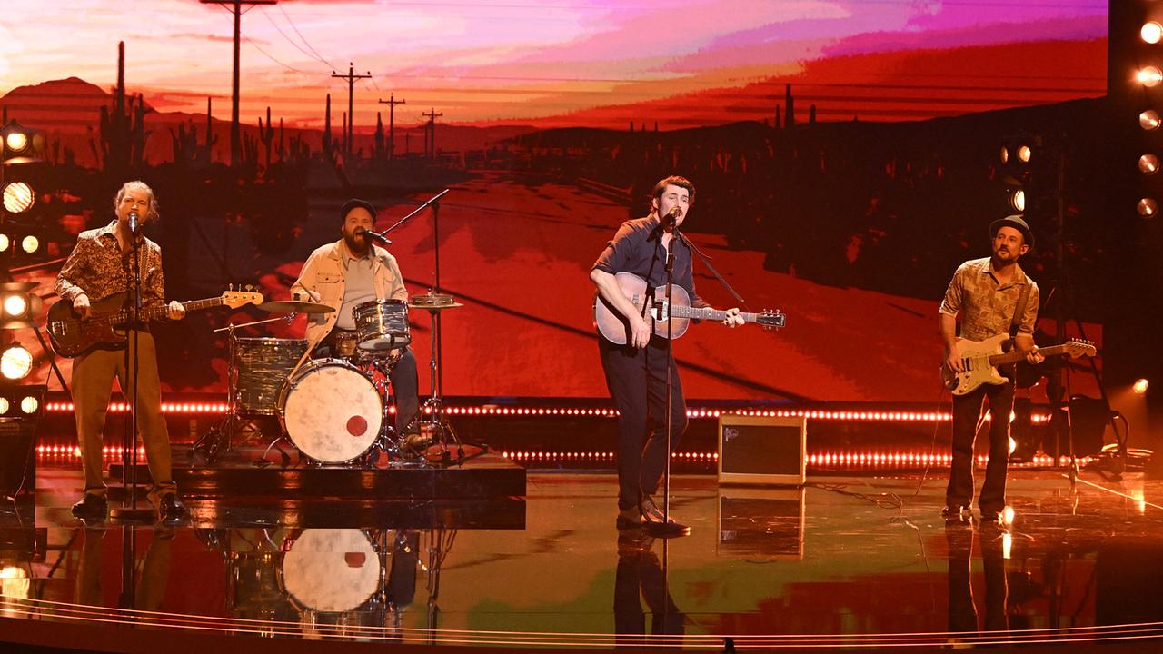 Die Band Reverend Stomp spielt vor einer Wüstenstraßen-Kulisse im Sonnenuntergang, mit Gitarren, Schlagzeug und warmem Bühnenlicht.