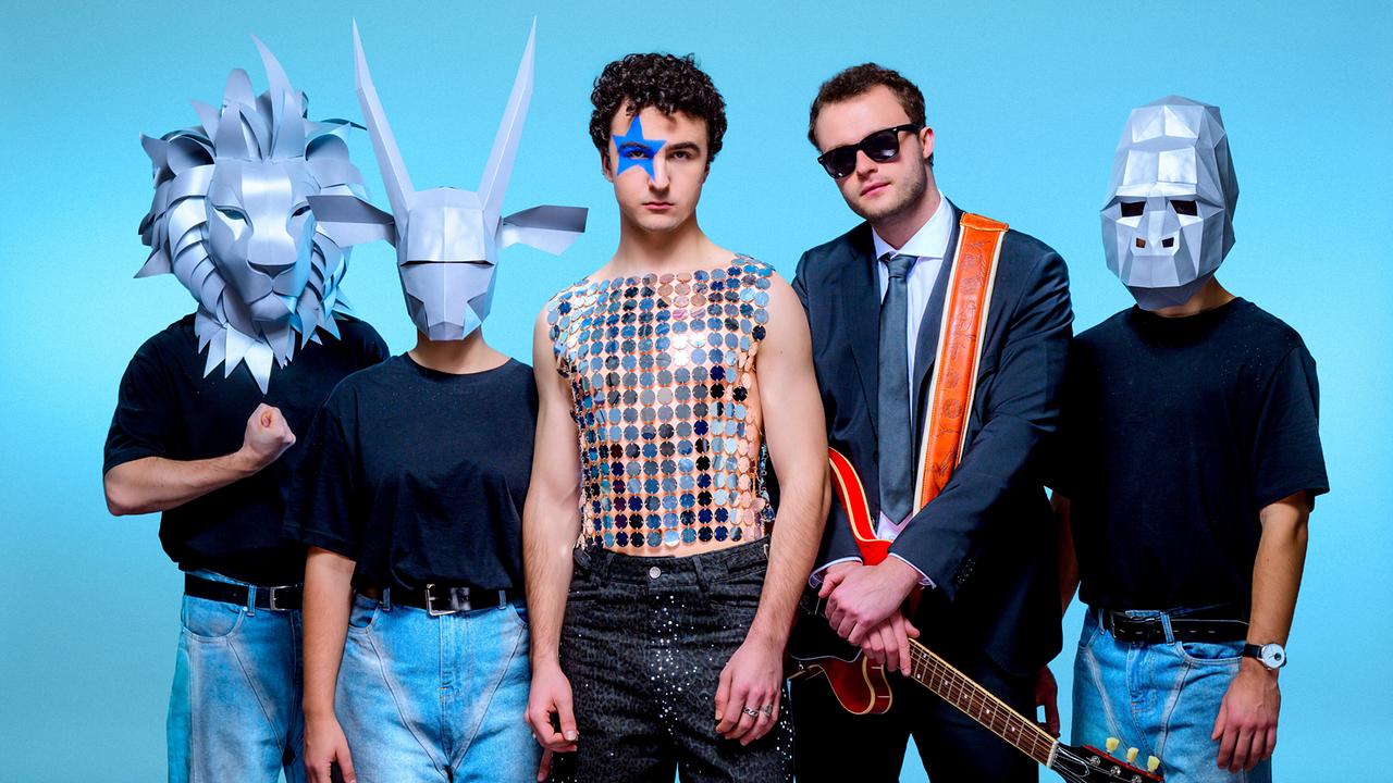 © ORF/Hans Leitner Die Gruppe Cosmó, bestehend aus fünf Männern, steht vor blauem Hintergrund, einige tragen fantasievolle Tiermasken, einer hält eine Gitarre, und der Sänger trägt ein metallisches Top und hat einen blauen Stern um sein rechtes Auge gemalt..