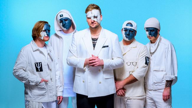 Die Gruppe FREVD bestehend aus fünf Männern posiert vor blauem Hintergrund in überwiegend weißen Outfits und blau-weißen Gesichtsmasken.