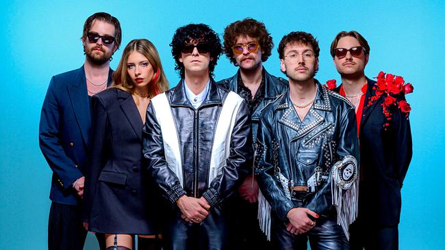 Nikotin mit weiteren 5 Bandmitgliedern präsentiert sich vor blauem Hintergrund in dunklen, teils ledernen und auffällig verzierten Bühnenoutfits.