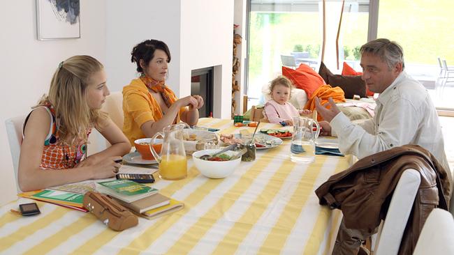 © ORF/Petro Domenigg Andreas Vitásek sitzt mit Lena, Valerie und einem kleinen Kind an einem großen Esstisch in einem hellen Zimmer beim Essen und unterhalten sich.