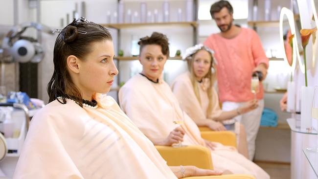 Caroline, Maria und Nicoletta sitzen nebeneinander in einem Friseursalon, während ihnen die Haare gestylt werden und ihnen von Francesco Sekt serviert wird.