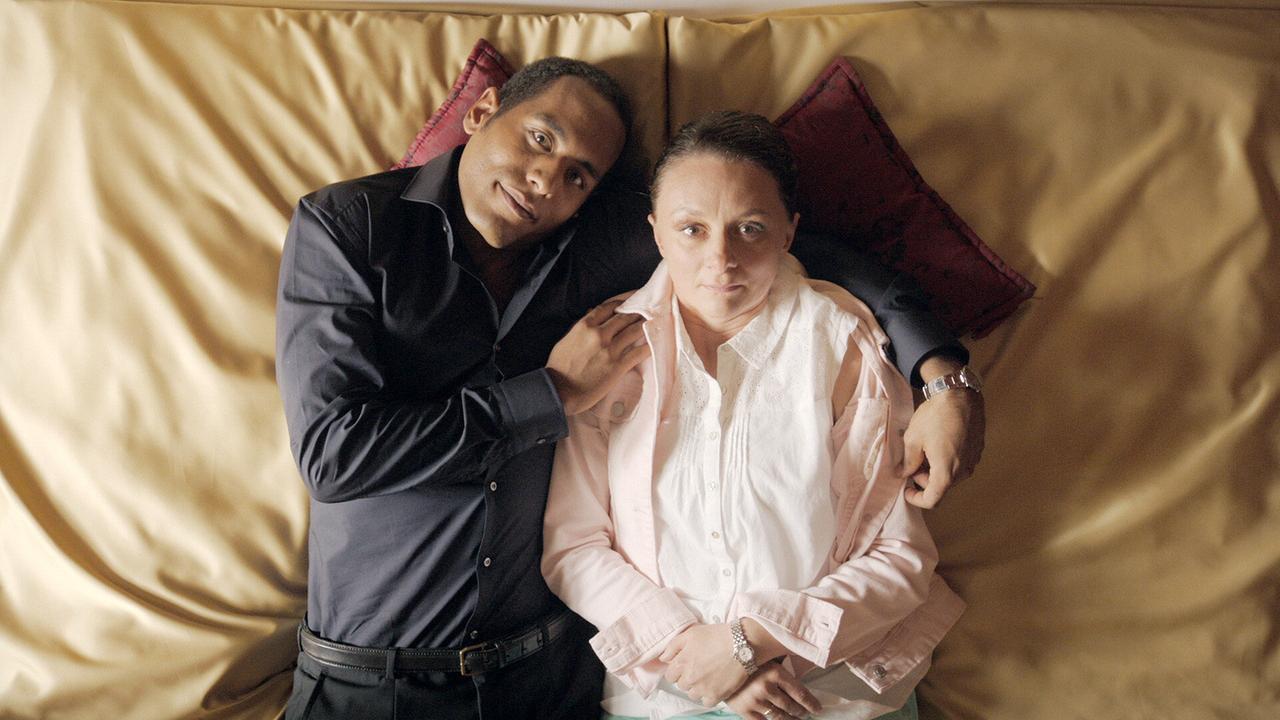 Timo und Maria liegen eng aneinander im Bett, wobei Timo liebevoll den Arm um Maria gelegt hat.