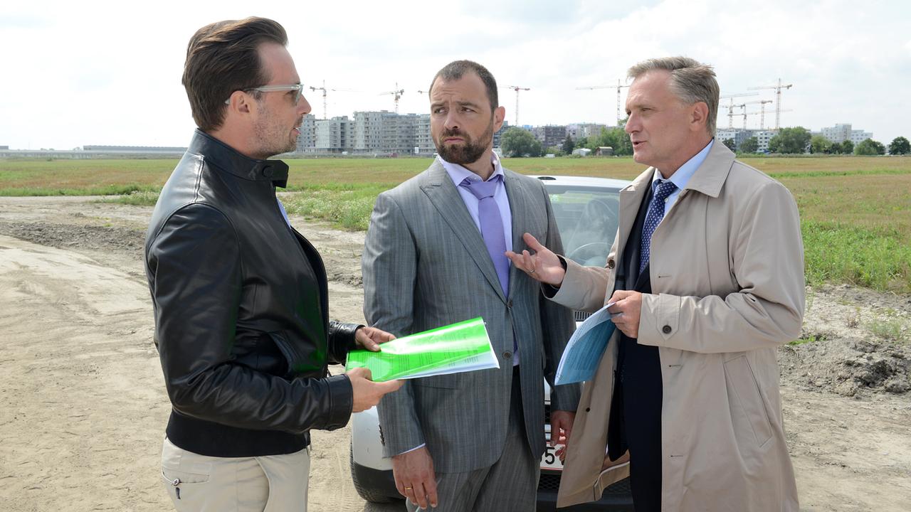© ORF/MR Film/Hubert Mican Bertram Selig, Georg Schneider und Hadrian Melzer stehen auf einem unbebauten Gelände vor einem Auto und diskutieren mit Unterlagen in der Hand über das Projektvorhaben.