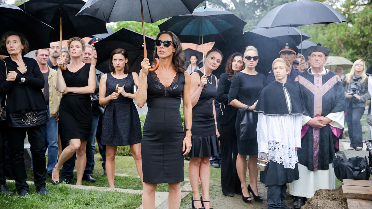 © ORF/MR Film/Petro Domenigg Eine Gruppe schwarz gekleideter Menschen, unter ihnen Anna, Sabine, Caroline, Waltraud, Maria, Tina und Nicoletta, steht bei einer Beerdigung bei Regen mit Regenschirmen auf einem Friedhof.