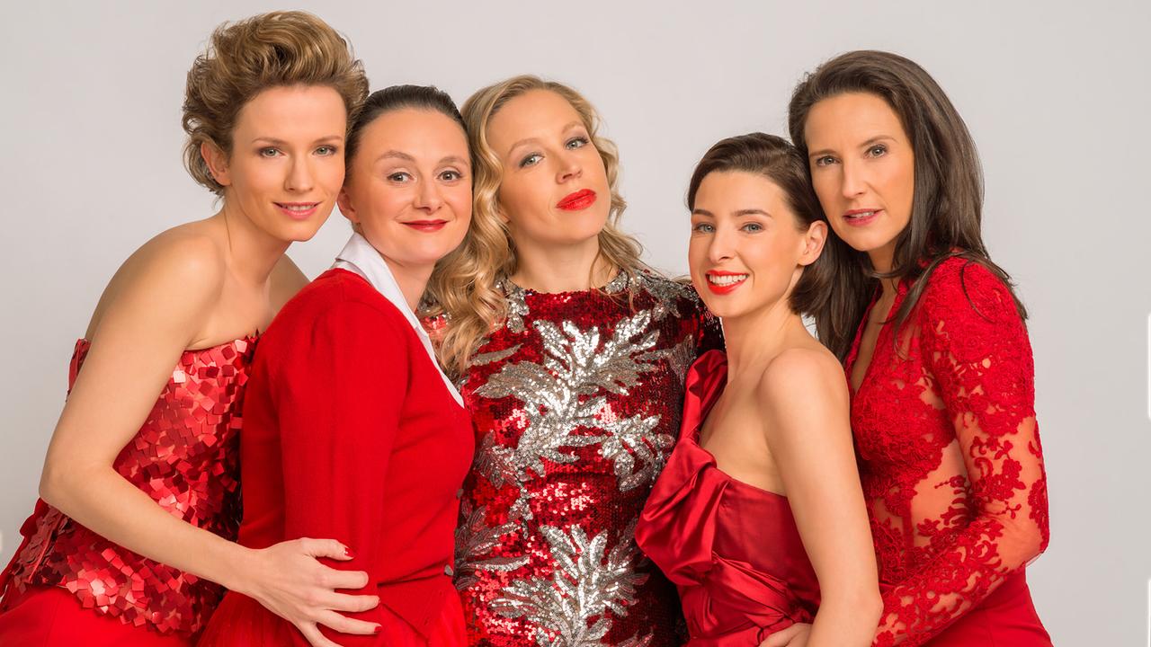 © ORF/Thomas Ramstorfer Adina Vetter, Gerti Drassl, Nina Proll, Martina Ebm und Maria Köstlinger posieren eng beisammen in eleganten roten Abendkleidern vor einem hellen Studiohintergrund.