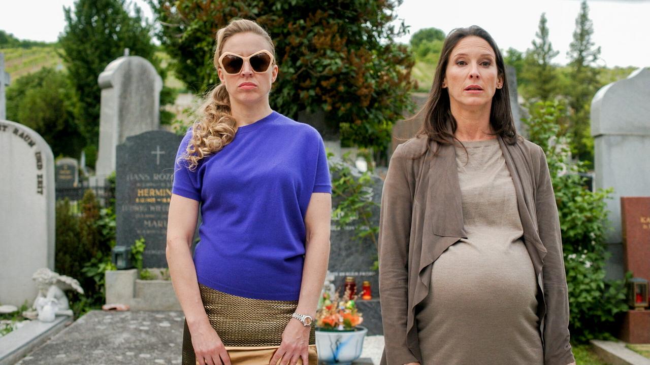 Nicoletta Huber und die schwangere Waltraud Steinberg stehen nebeneinander auf einem Friedhof und blicken ernst nach vorne.