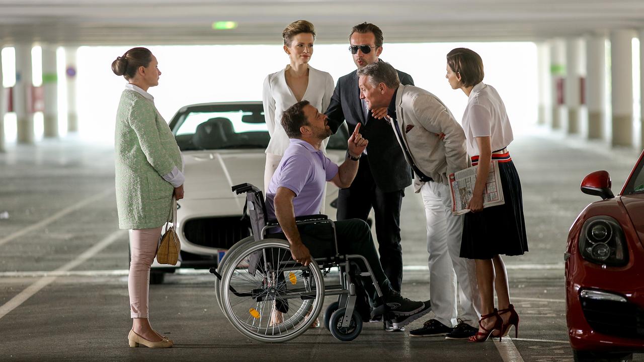 In einer Tiefgarage zwischen zwei Autos diskutiert Georg Schneider im Rollstuhl mit Hadrian Melzer. Um sie herum stehen Maria Schneider, Sabine Herold, Bertram Selig und Caroline Melzer. 