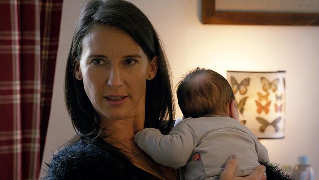 Nahaufnahme von Waltraud, die in einem Wohnraum ein Baby auf dem Arm trägt.