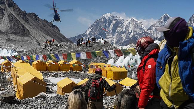 © ORF/SRF/One Gate Basis Camp am Mount Everest, im Hintergrund die schneebedeckten Gipfel, im Vordergrund dicht aneinander gereihte gelbe Biwak-Zelte, ein Hubschreuaber fliegt darüber hinweg
