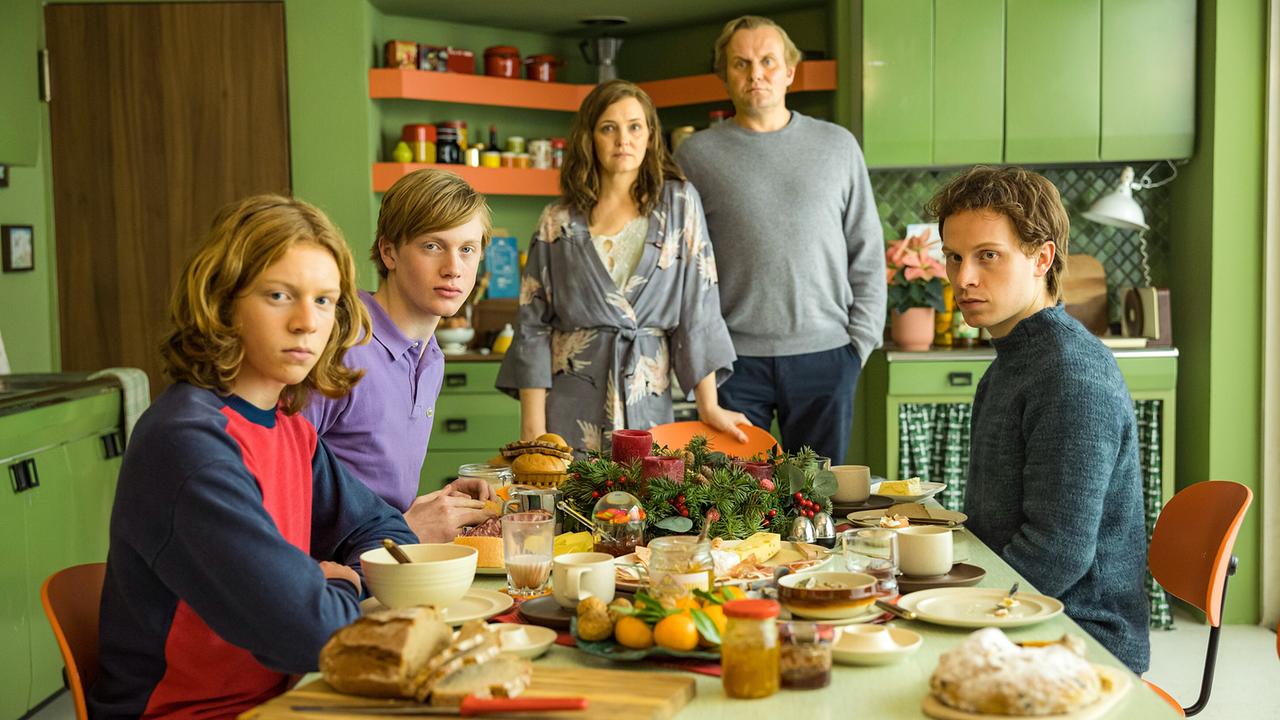 © ORF/Warner Bros. Entertainment Inc. Joachim sitzt mit seinen Brüdern am Frühstückstisch, hinter ihnen stehen seine Eltern, alle blicken für ein Gruppenbild in die Kamera