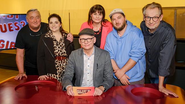 In einem TV‑Studio sitzen und stehen Andreas Vitásek, Isabell Pannagl, Oliver Baier, Eva Maria Marold, David Scheid und Severin Groebner um einen roten Tisch, im Hintergrund ist ein Bildschirm mit „Was gibt es Neues?“ zu sehen.