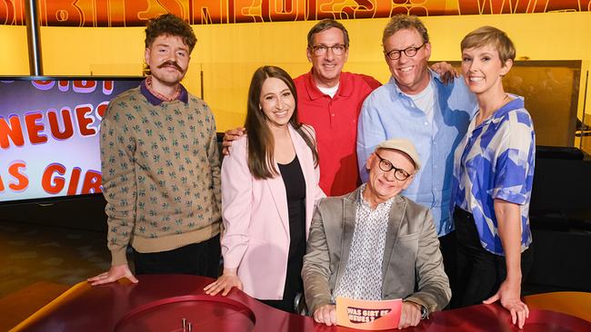 Benedikt Mitmannsgruber,  Lydia Prenner-Kasper,  Viktor Gernot, Herbert Steinböck und Sonja Pikart stehen im TV-Studio rund um Oliver Baier, der am Moderatorenpult in der Mitte sitzt und eine Karte mit der Aufschrift „Was gibt es Neues?“ in der Hand hält.