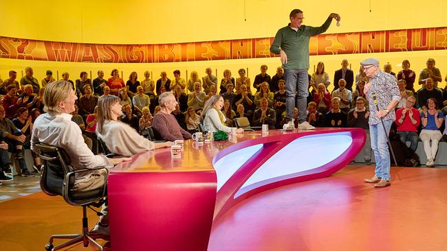 Im "Was gibt es Neues?"-Studio steht Viktor Gernot auf dem Tisch des Rateteams vor Oliver Baier, während die Zuschauerinnen und Zuschauer im Studio applaudieren und Gery Seidl, Eva Maria Marold, Thomas Maurer und Lydia Prenner-Kasper daneben sitzen.
